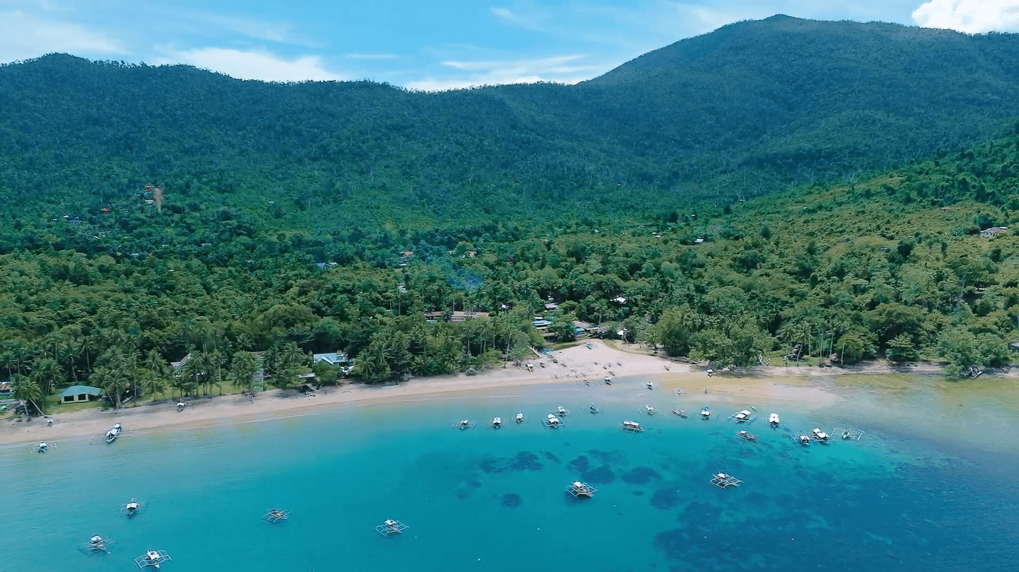 Turquoise bay with small boats, a beach, and forested hills